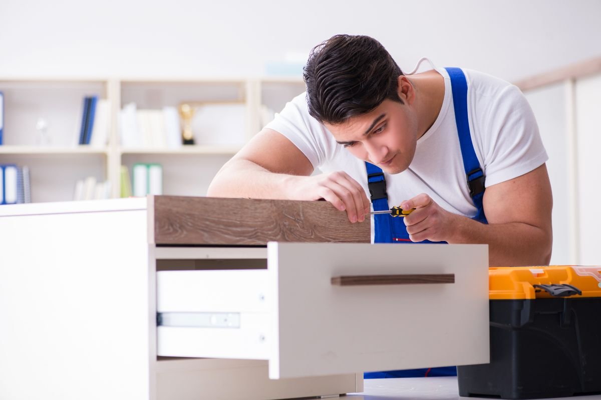 A man in overalls repairs a wooden drawer as part of a furniture repair service.