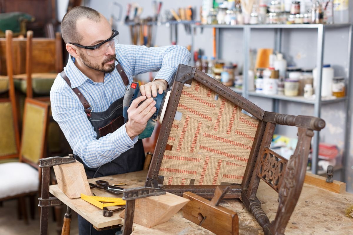 A man repairs a chair in a workshop, showcasing his skills in furniture restoration.