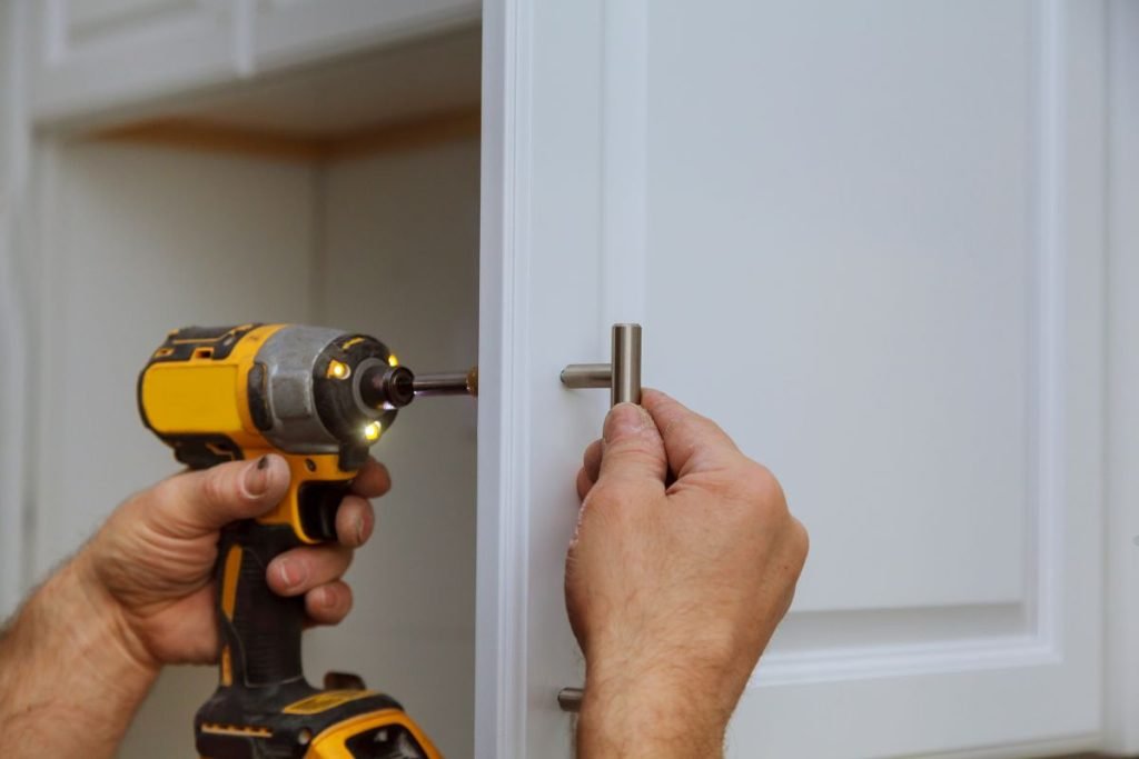 A man operates a drill to install a cabinet door as part of a furniture repair service.