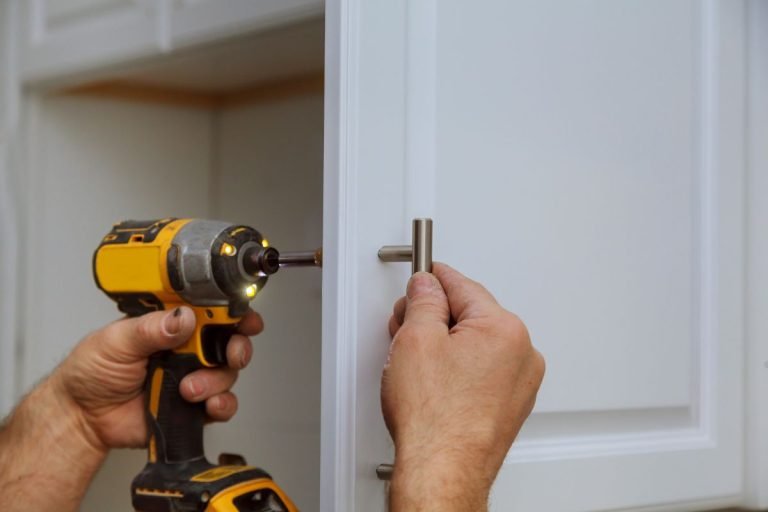 A man operates a drill to install a cabinet door as part of a furniture repair service.
